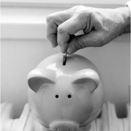 A hand puts a coin into a piggy bank resting on a radiator